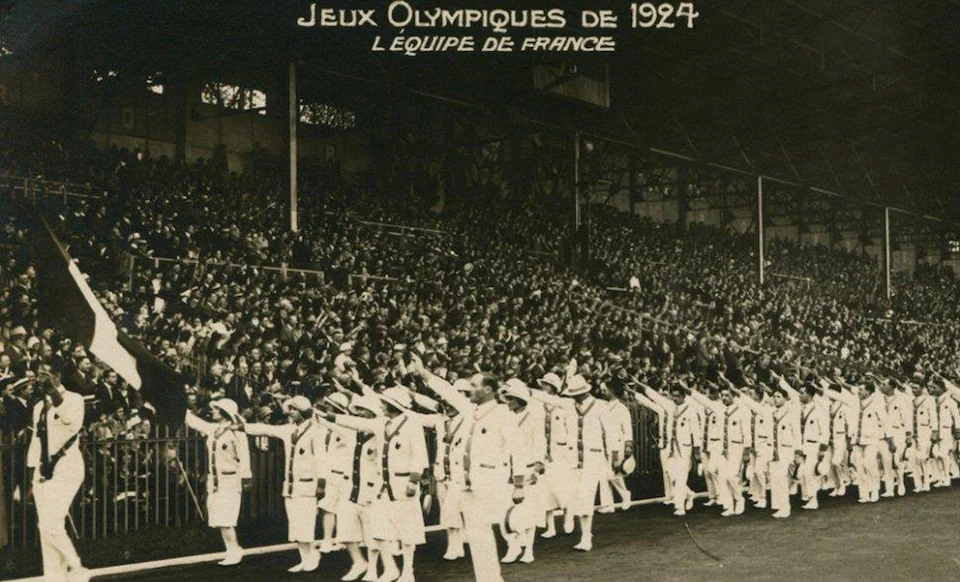 Sur la photo en noir et blanc, les athlètes défilent devant les gradins.