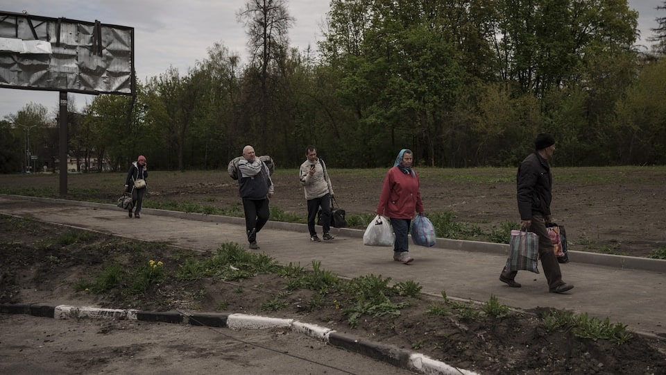 Ukrainians holding bags with their belongings walk in line. 