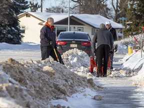 Neighbors Dana Sydor, Isa Khurshed, and Nizam Khurshed clear the windrows from in font of their homes shortly after a grader had created them on Wednesday, Jan. 12, 2022 in north Edmonton.
