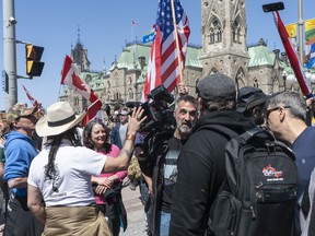 A crowd of demonstrators confront a journalist on Wellington St. in front of Parliament Hill.