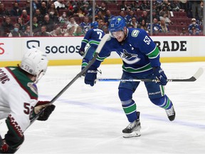 Michael Carcone of the Arizona Coyotes looks on as Bo Horvat of the Vancouver Canucks winces while skating to the bench after getting hit in the ankle with the puck during their NHL game at Rogers Arena April 14, 2022 in Vancouver.