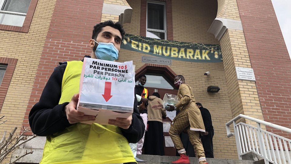 A person with a box to collect donations in front of a mosque.