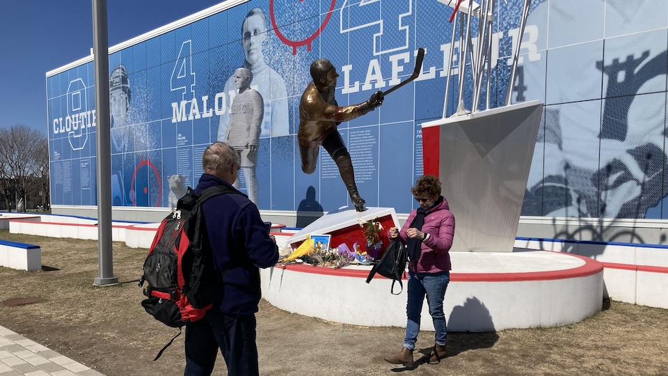 A man and a woman stand near a public work of art representing Guy Lafleur.