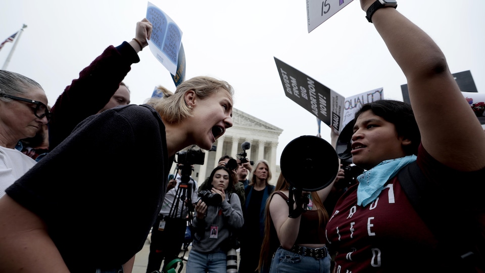 Two groups of women oppose each other, placards in hand, and chant slogans in front of the media gathered in front of the Supreme Court building. 