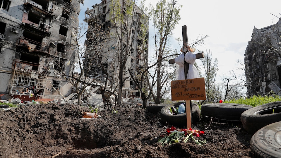 A cross on which one can read, in Russian, the name of “Kolesnikov Anatoly Ivanovich”, in front of buildings destroyed by the bombardments. 