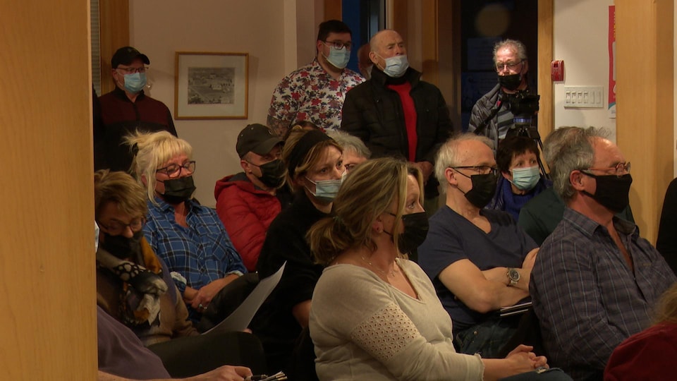 In the municipal council chamber of Percé, several people wearing a mask are seated or standing for lack of space.