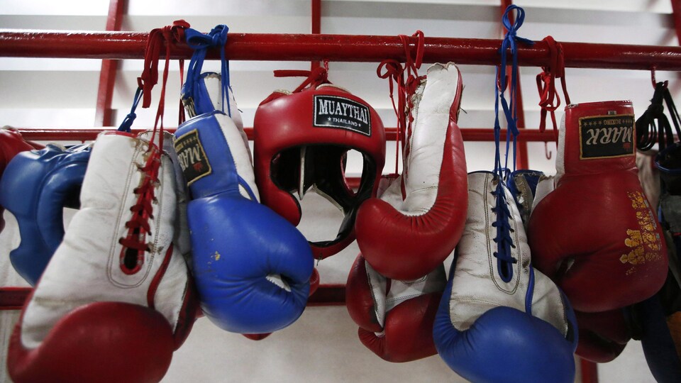 Blue and red boxing gloves hang on a metal rod.  A red boxing helmet is also hung there.