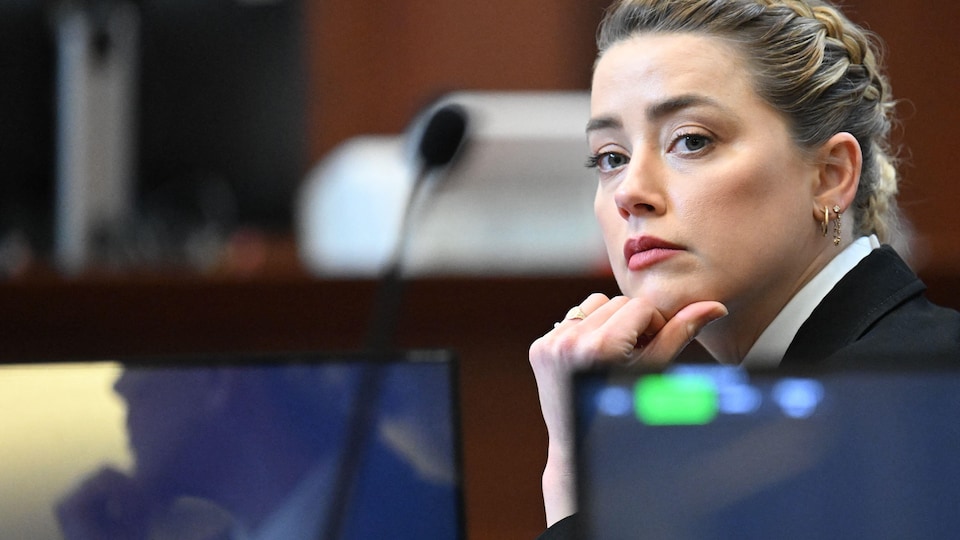 Amber Heard, hand on chin, seated in front of a microphone.