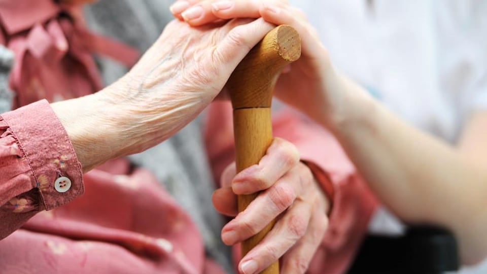 The hand of a nurse rests on that of an elder. 