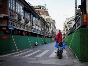 A delivery worker standing on a scooter looks over barriers in a closed residential area during lockdown, amid the COVID-19 pandemic, in Shanghai, China, May 9, 2022.
