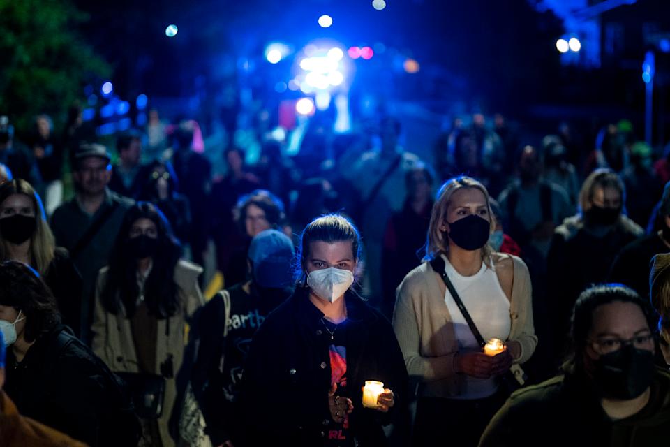 Two women wearing surgical masks, flanked by other protesters, hold candlelight vigil in the dark.