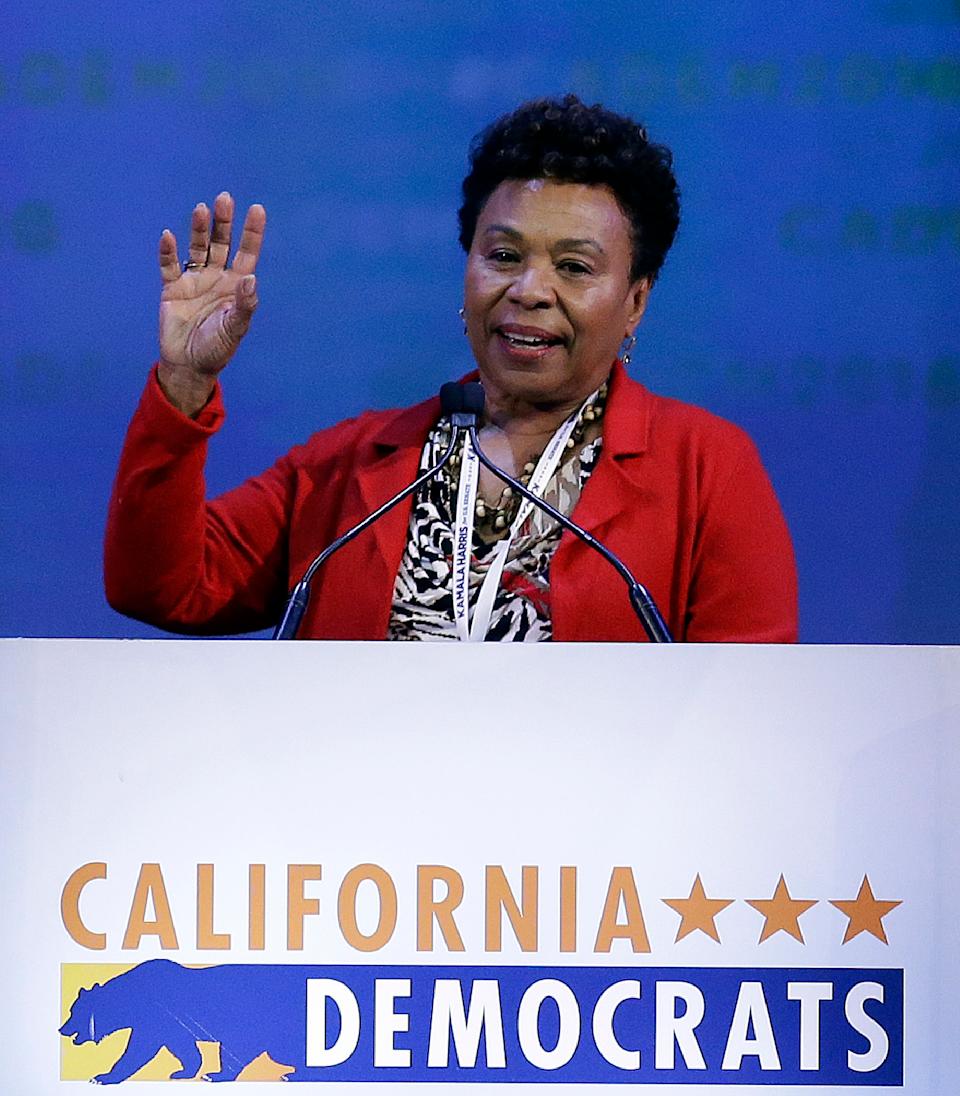 Rep. Barbara Lee waves as she speaks into the microphone over a banner that reads California Democrats and displays the state symbol, a grizzly bear.