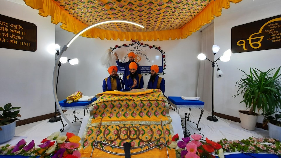 Four men in orange turbans sing in a Sikh temple.