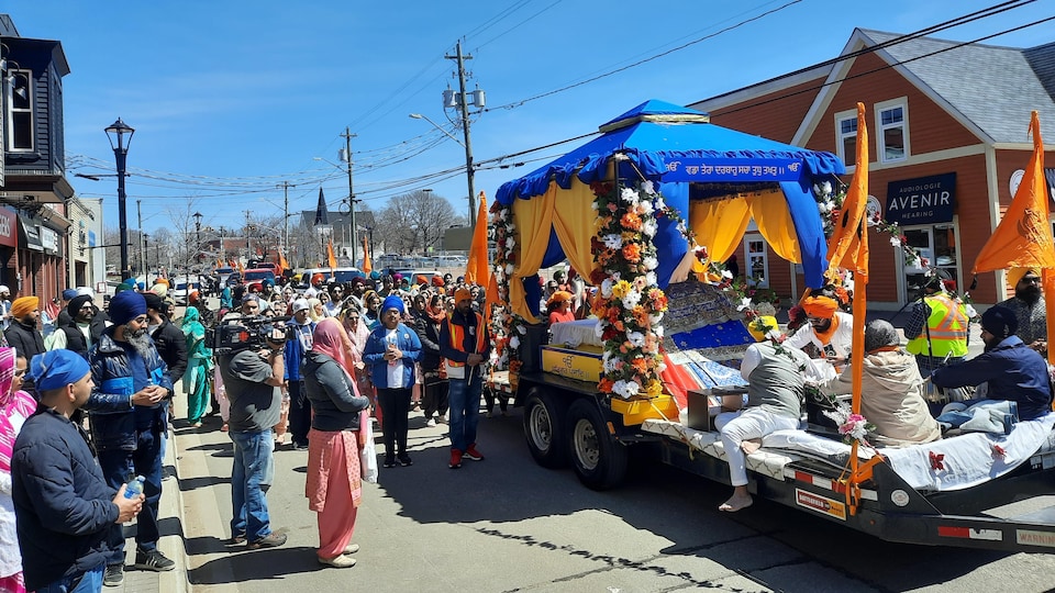 A float decorated with flowers and orange flags is followed by a walking crowd. 