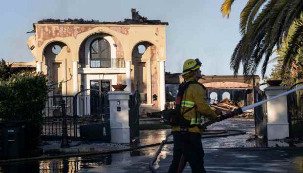 A firefighter sprays an adjacent house after the Coastal fire...
