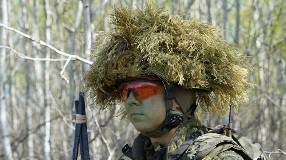 A soldier wears a helmet on which is placed equipment allowing him to blend into his environment.