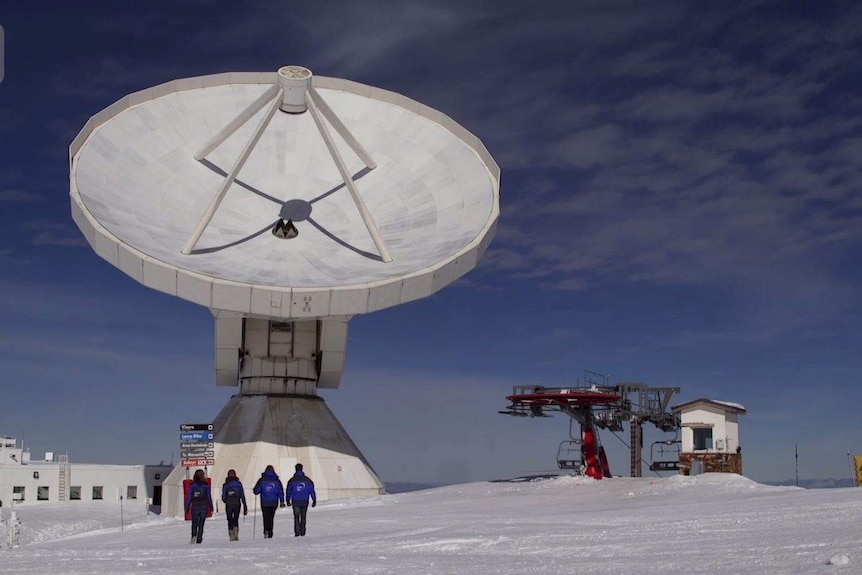 A giant telescope with people walking in front of it on the snow.