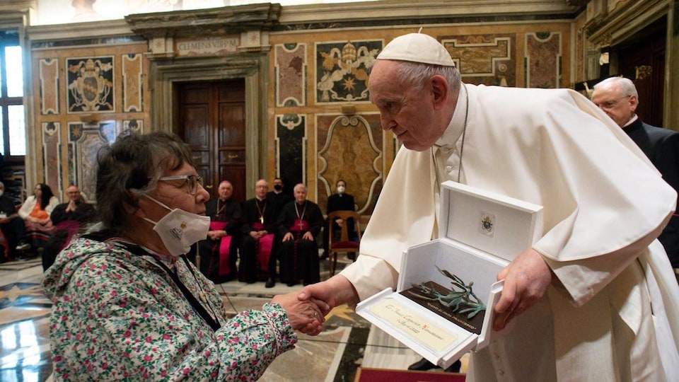 Le pape tient dans une main une écrin contenant une sculpture et serre de l'autre main celle d'une femme.
