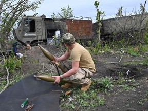 A Ukrainian serviceman inspects an abandoned munitions next to a destroyed Russian military vehicle near the village of Mala Rogan east of Kharkiv, on May 13, 2022, amid Russian invasion of Ukraine.