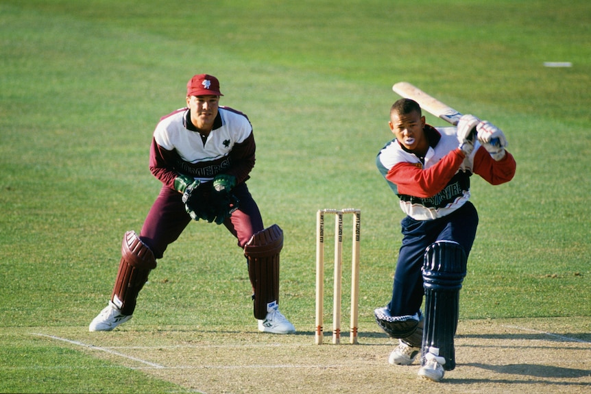 A young Andrew Symonds plays a shot.  He wears colorful clothes and does not wear a helmet.