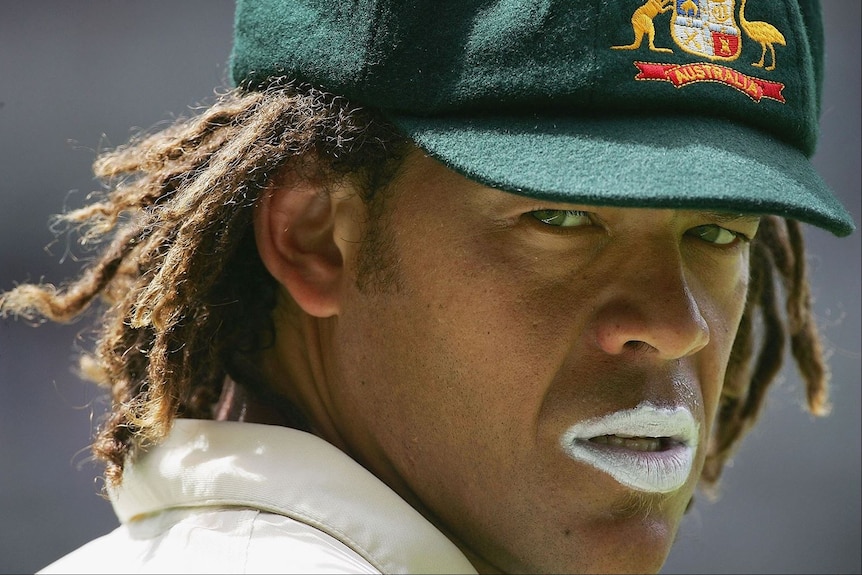 Close-up photograph of Andrew Symonds, wearing a baggy green cap, dreadlocks, and white zinc on both lips