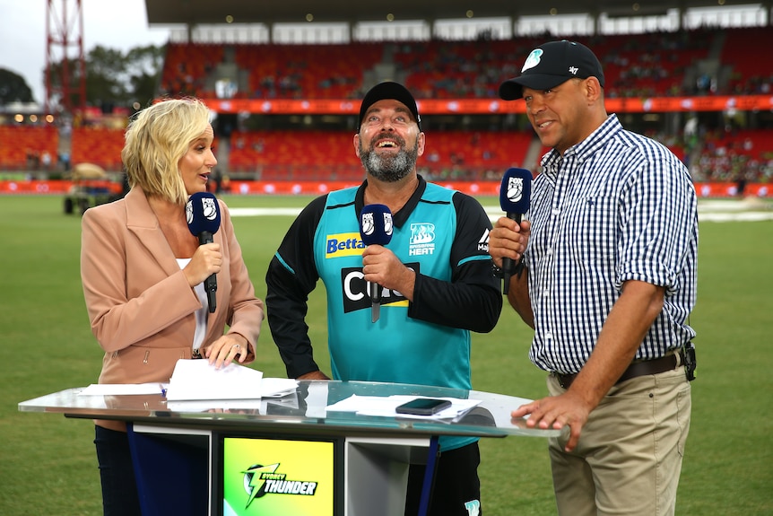 Andrew Symonds holds a microphone with Darren Lehmann and Jessica Yates
