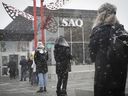 Customers brave the falling snow as they wait in line to enter the SAQ store at the Jean-Talon Market on March 23, 2020.