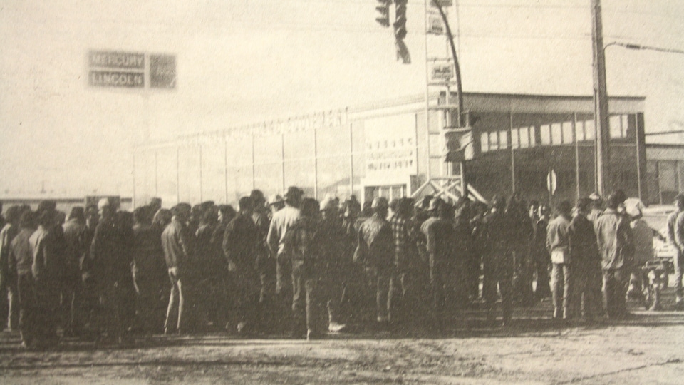 In a file photo, a crowd of workers are gathered in front of a building.