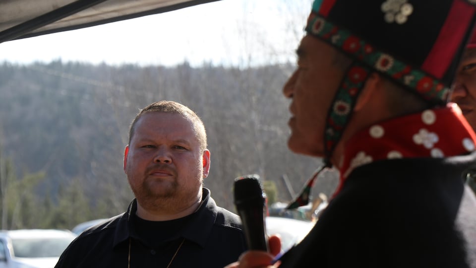 A man from the front listens to another man who is seen out of focus and who speaks with a microphone.