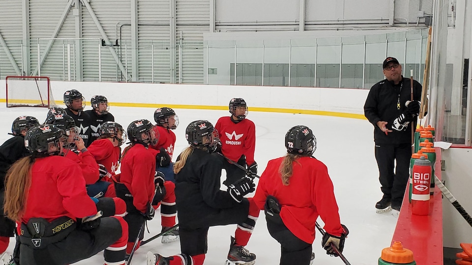 The hockey group is gathered on the ice near the coach to receive his advice.