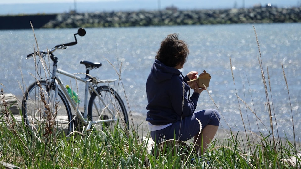 A woman on a bicycle stopped for a bite to eat while looking out to sea.
