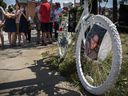 A photo of Louis Morency is attached to a ghost bike at the corner of Christophe-Colomb Ave. and Mistral St. in Montreal on July 24, 2021, as his surviving wife and daughters look on.  His wife, Marie-Soleil Giguère is holding Delphine (left) and Jeanne, at an event to commemorate the life of Louis, who died at the intersection when he was hit by a truck while cycling nine years ago.