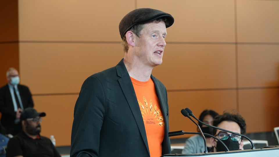 A man wearing a cap speaks into the microphone.