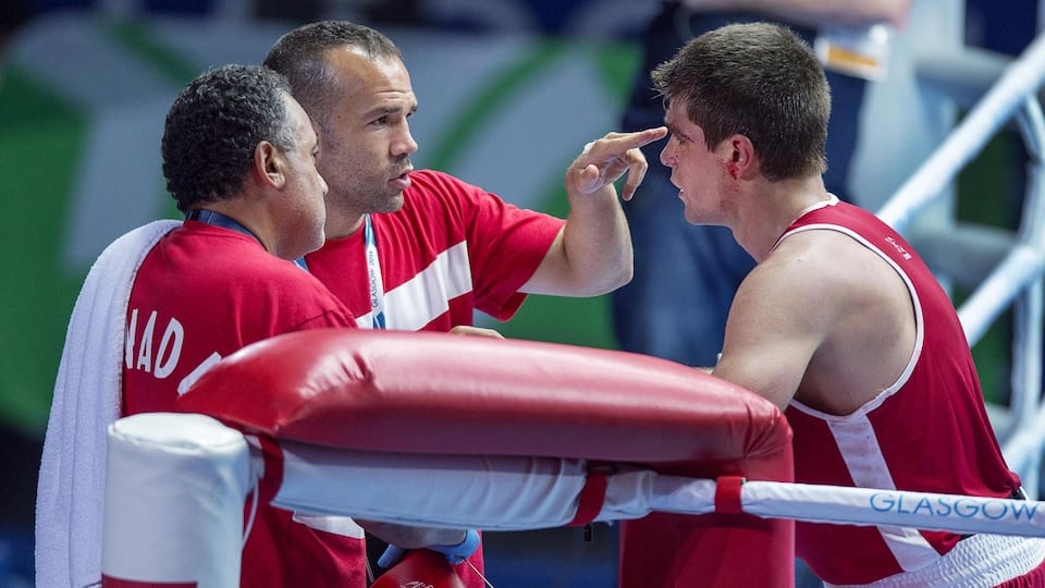 A boxing trainer, dressed in red, offers advice by pointing his index finger to his athlete's forehead in a ring. 