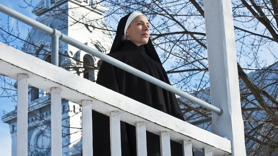 A nun gazes into the distance, on a balcony.