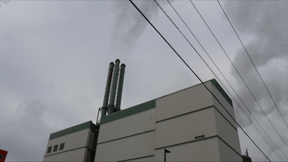An industrial building surmounted by four chimneys from which smoke escapes.