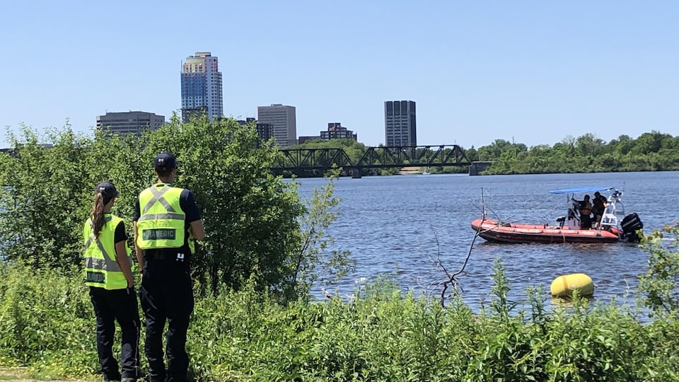 Two paramedics scan the Ottawa River on which an emergency services boat is circulating. 