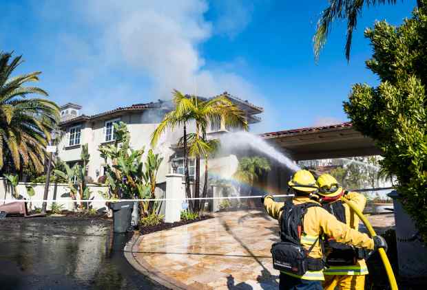 A firefighter sprays an adjacent house after the Coastal fire...