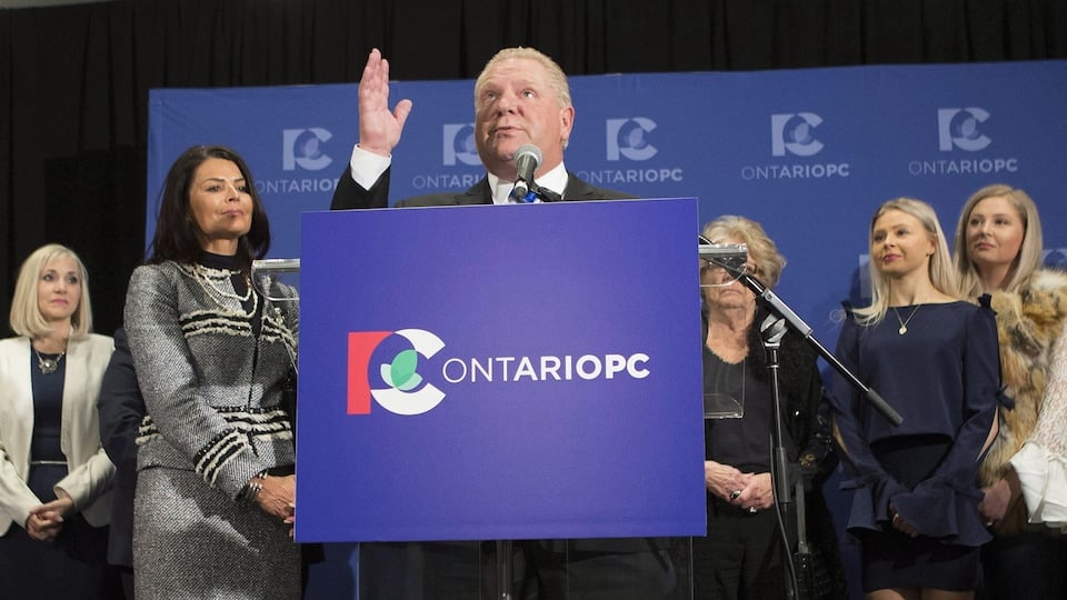 Doug Ford looks up at the sky and holds one hand in the air.