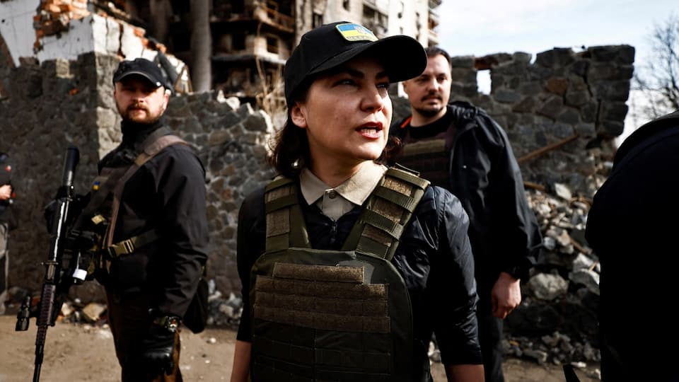 Iryna Venediktova, wearing a cap and a bulletproof vest, in a landscape of destruction.
