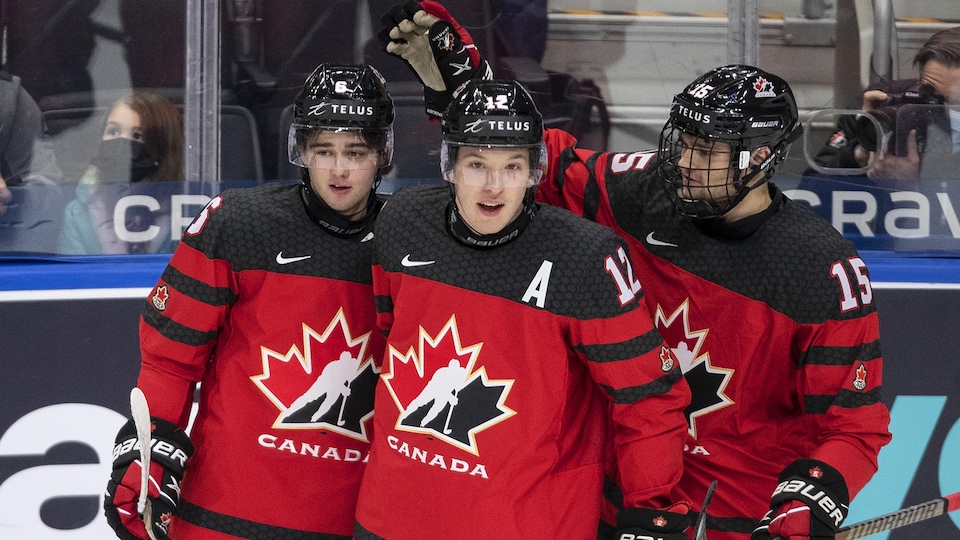 Three Canada players in red and black uniforms after celebrating a goal.