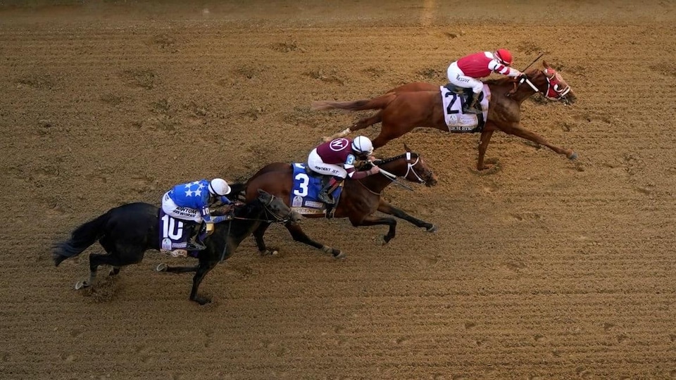 Three horses on a dirt track at the Kentucky Derby at Churchill Downs, May 7, 2022.
