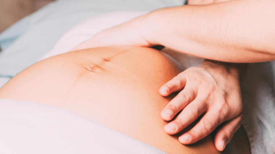 Two female hands on the belly of a pregnant woman lying on her back.