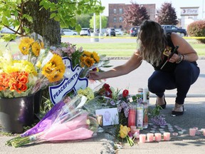 A mourner crouches by flowers and candles, during a vigil for victims of the shooting at a TOPS supermarket in Buffalo, NY, Sunday, May 15, 2022.
