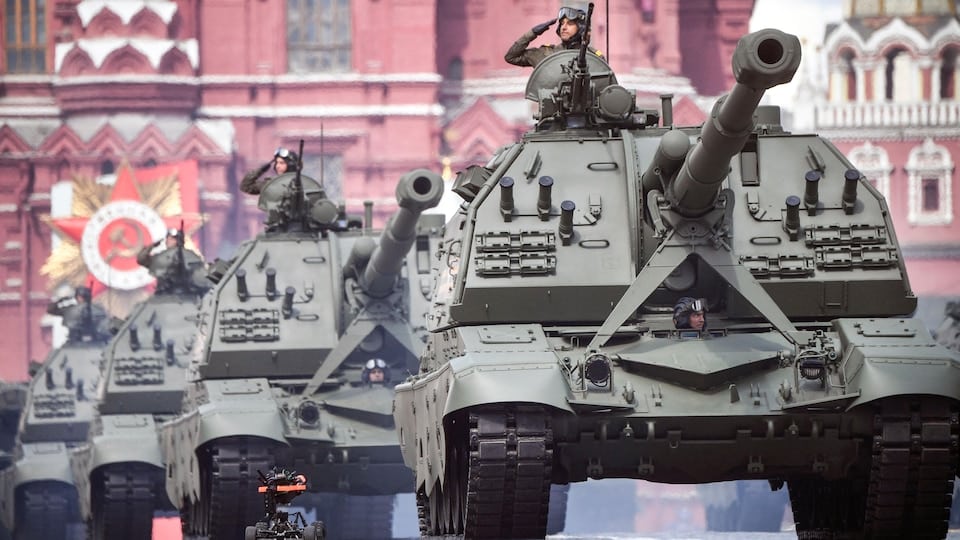 An armored vehicle drives on Red Square.  Soldiers taking their places there give a military salute. 
