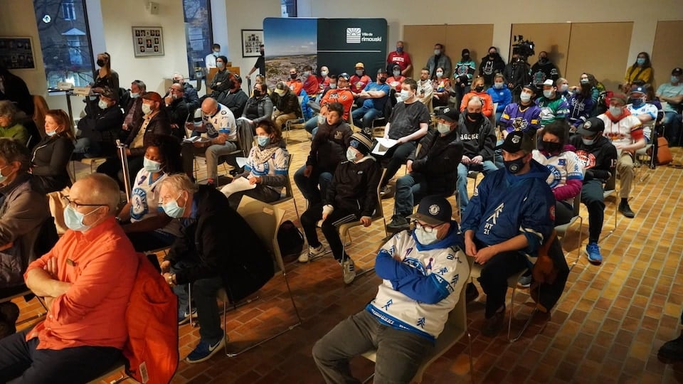 People sitting in the city council chamber with hockey jerseys.