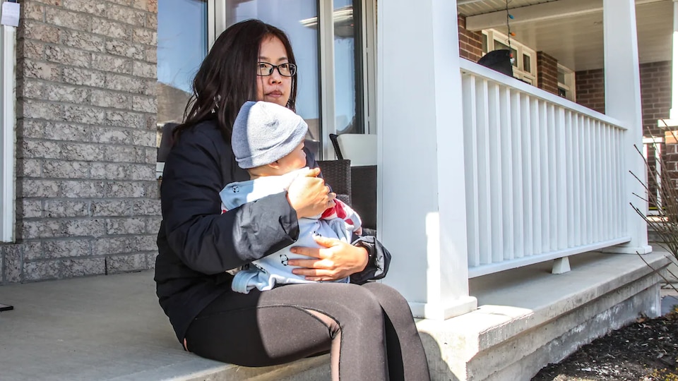 A woman sitting on the porch of her house with a baby in her arms.