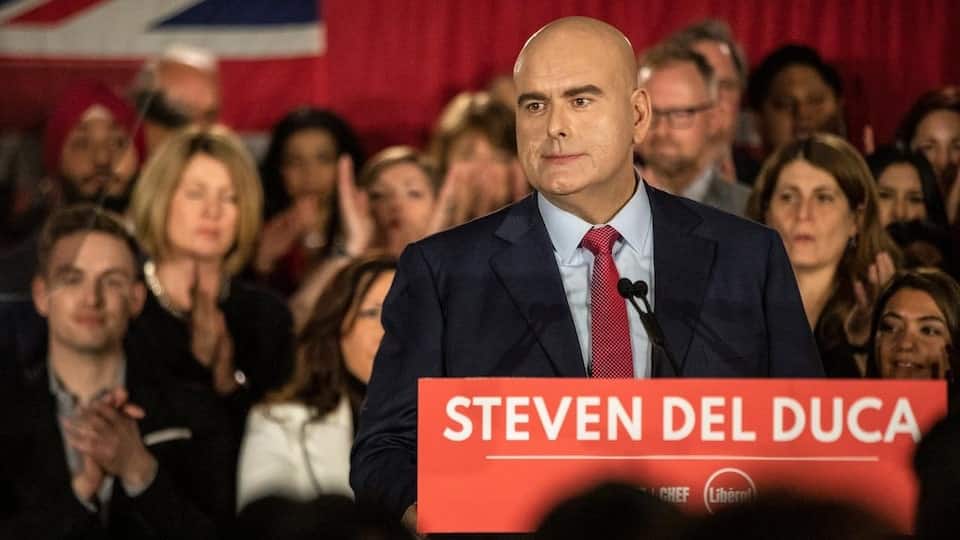 Steven Del Duca on a podium surrounded by supporters.