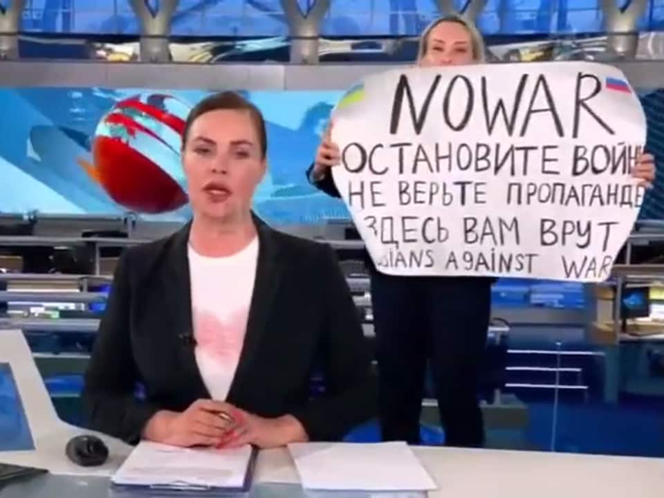 A woman, who popped up on a television set, holds a sign saying, “No to war.  Don't believe the propaganda.  You are being lied to here,” behind a newsreader. 