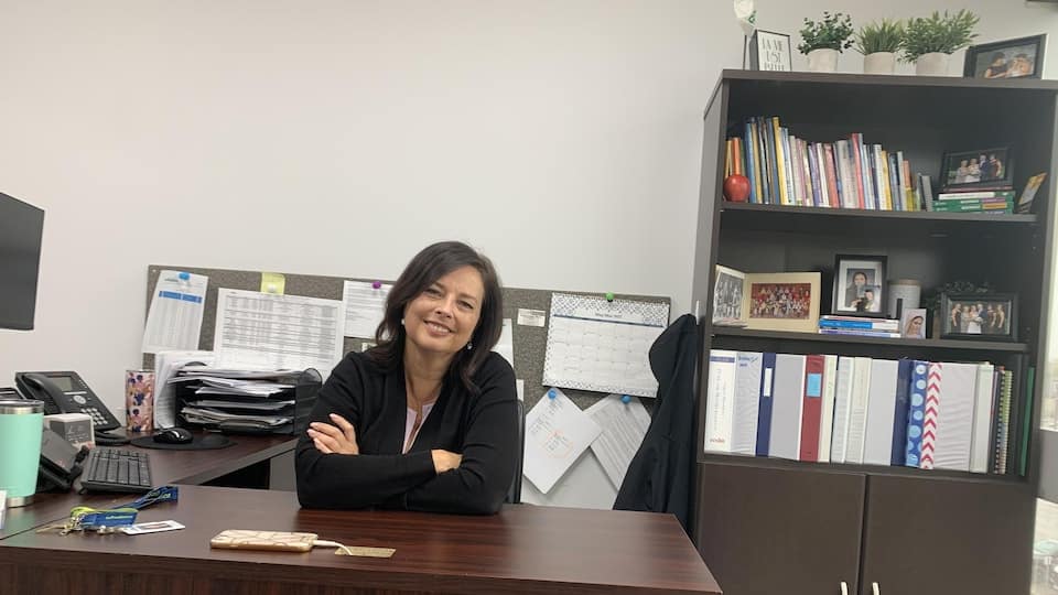 Jeannine Duguay Pellerin, Principal of Sainte-Trinité Catholic Secondary School in Windsor, is sitting in her office, smiling.  She has her arms crossed and looks straight at the camera.